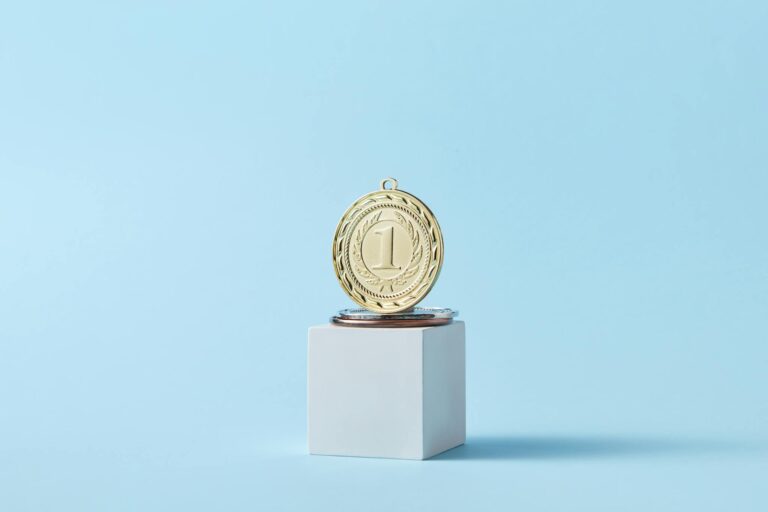 Close-up of a gold medal on a podium with a baby blue background, symbolizing victory.