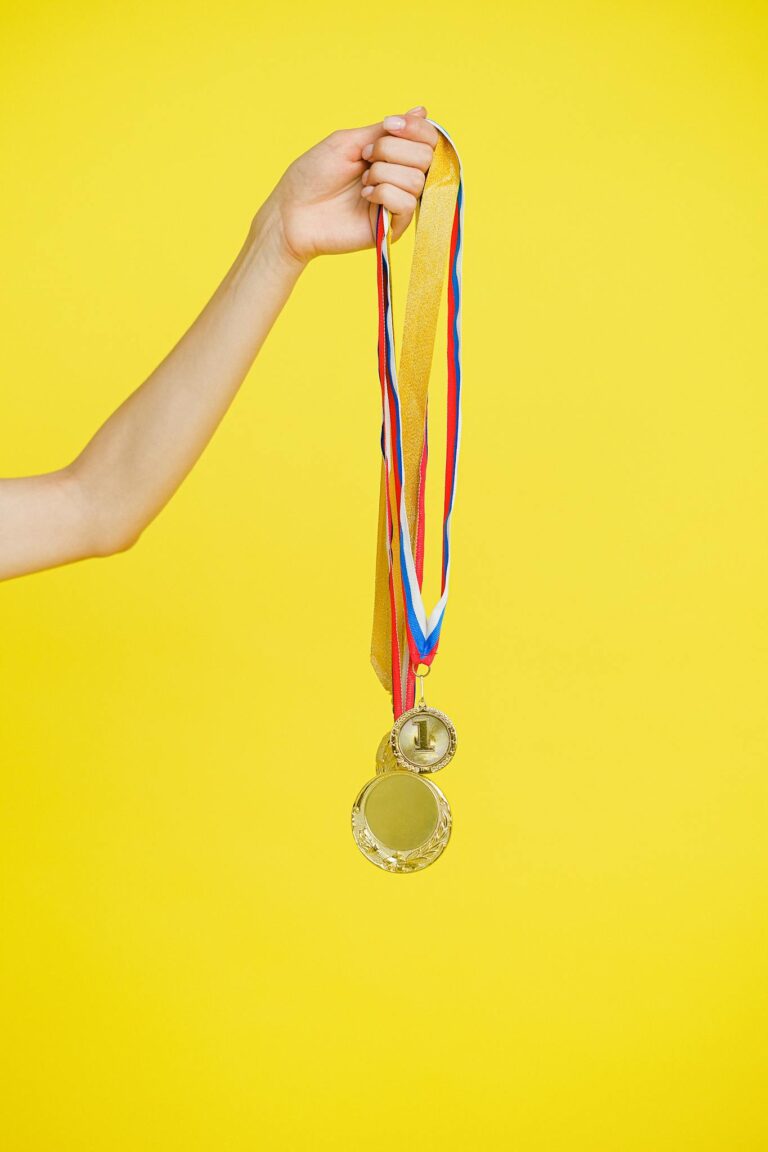 Close-up of a hand holding gold medals symbolizing victory and achievement against a vibrant yellow backdrop.