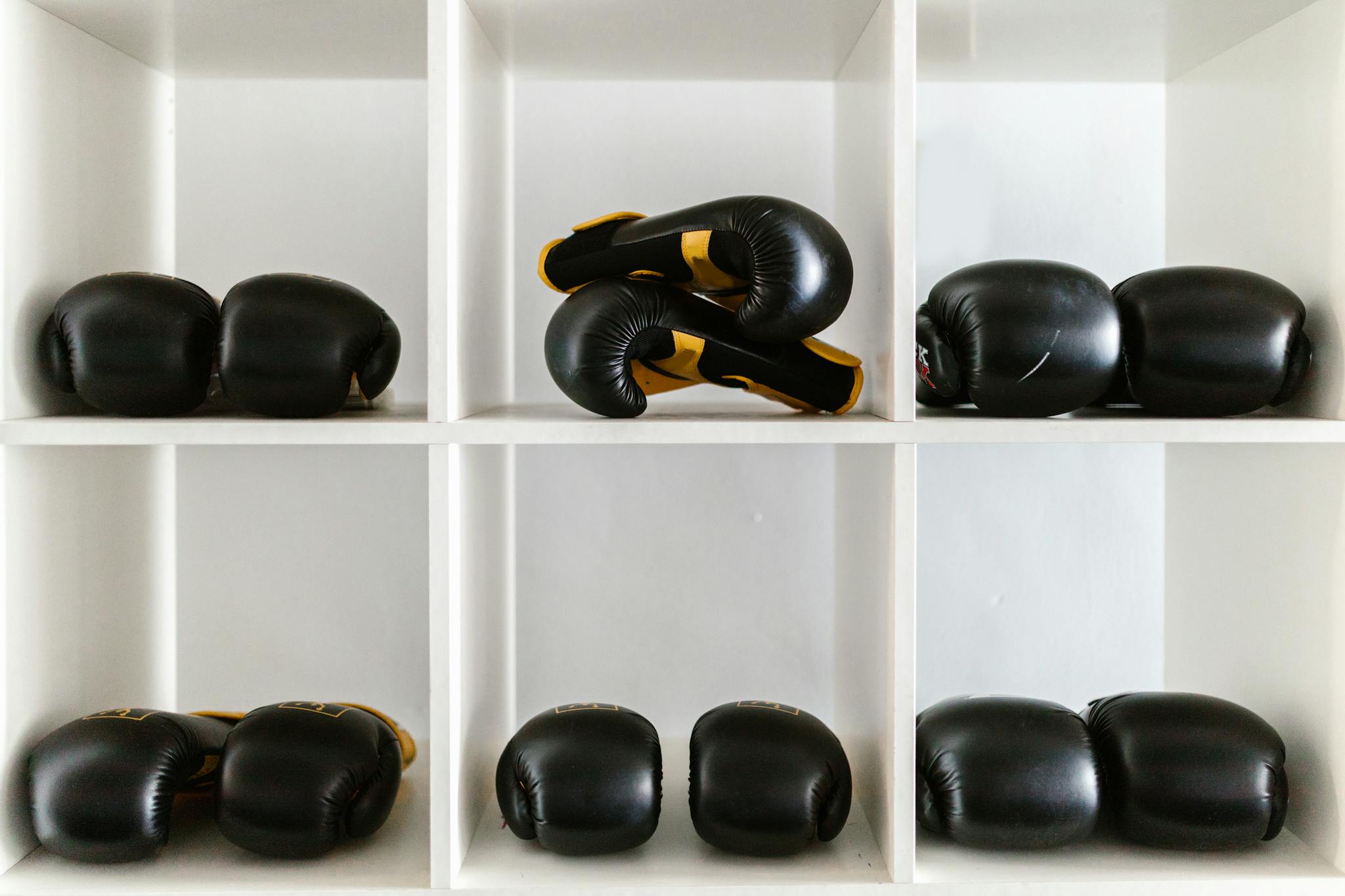 Neatly arranged black boxing gloves on a white shelf, ready for training.