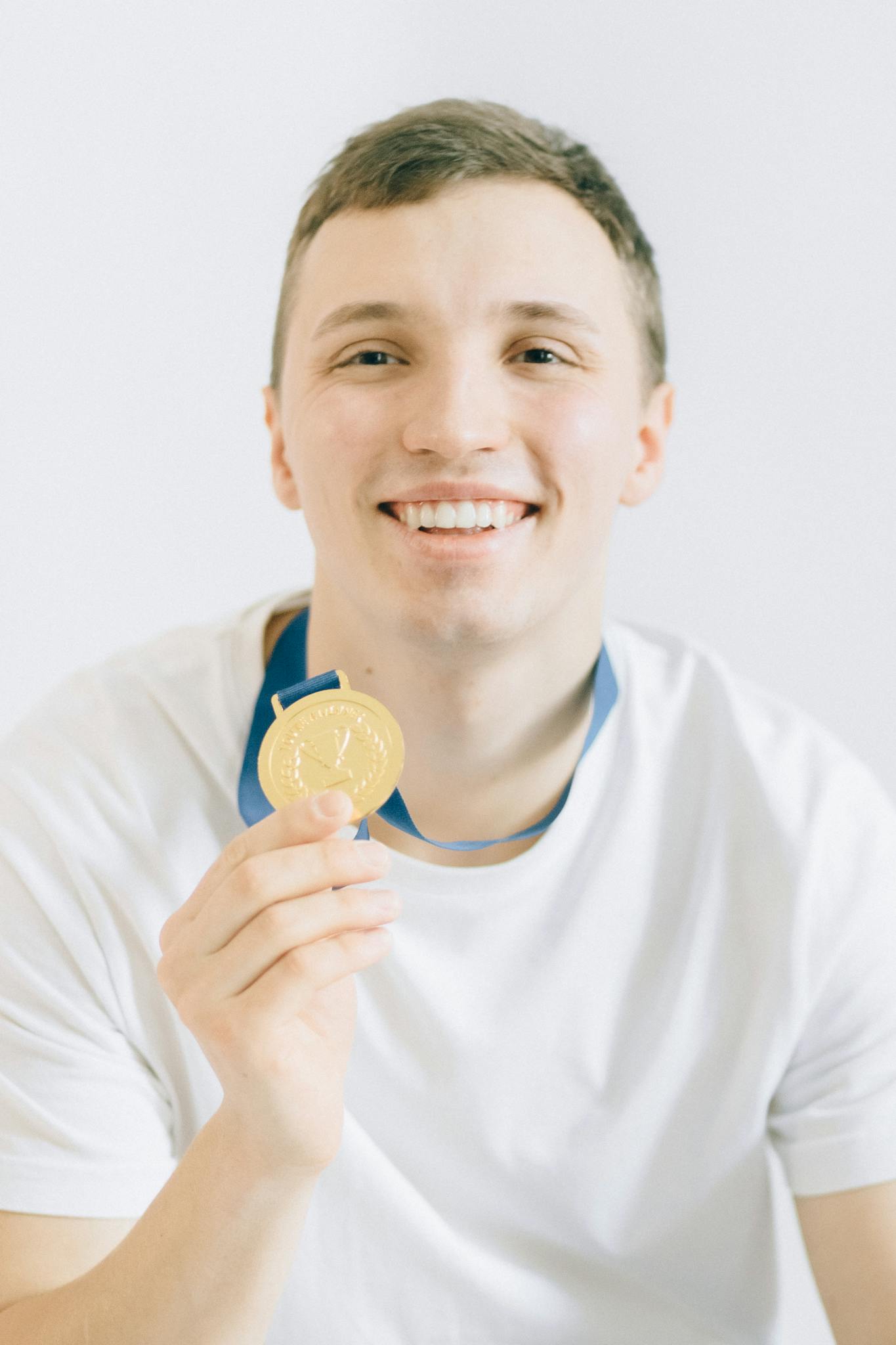 Smiling athlete proudly holds a gold medal, showcasing achievement and joy.